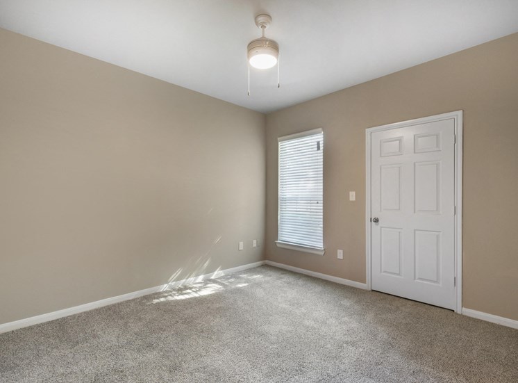 Living room with white door, window with blinds, wall to wall carpet, and tan walls